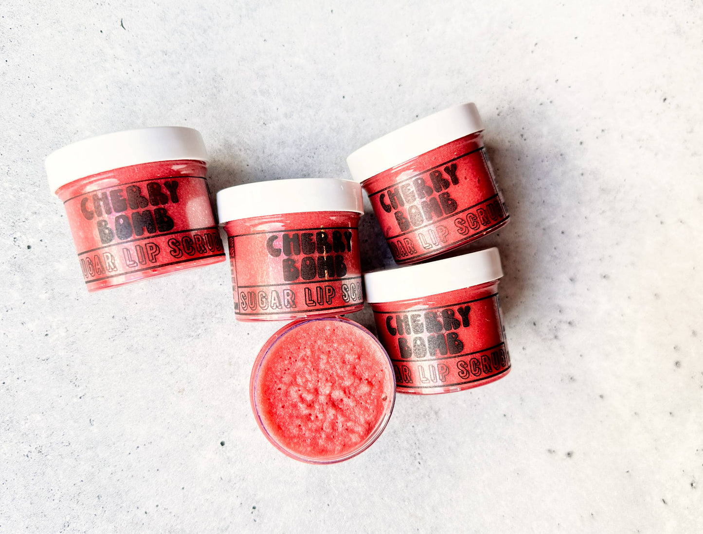 Red lip scrubs with 'Cheeky Buns' branding on a light gray surface