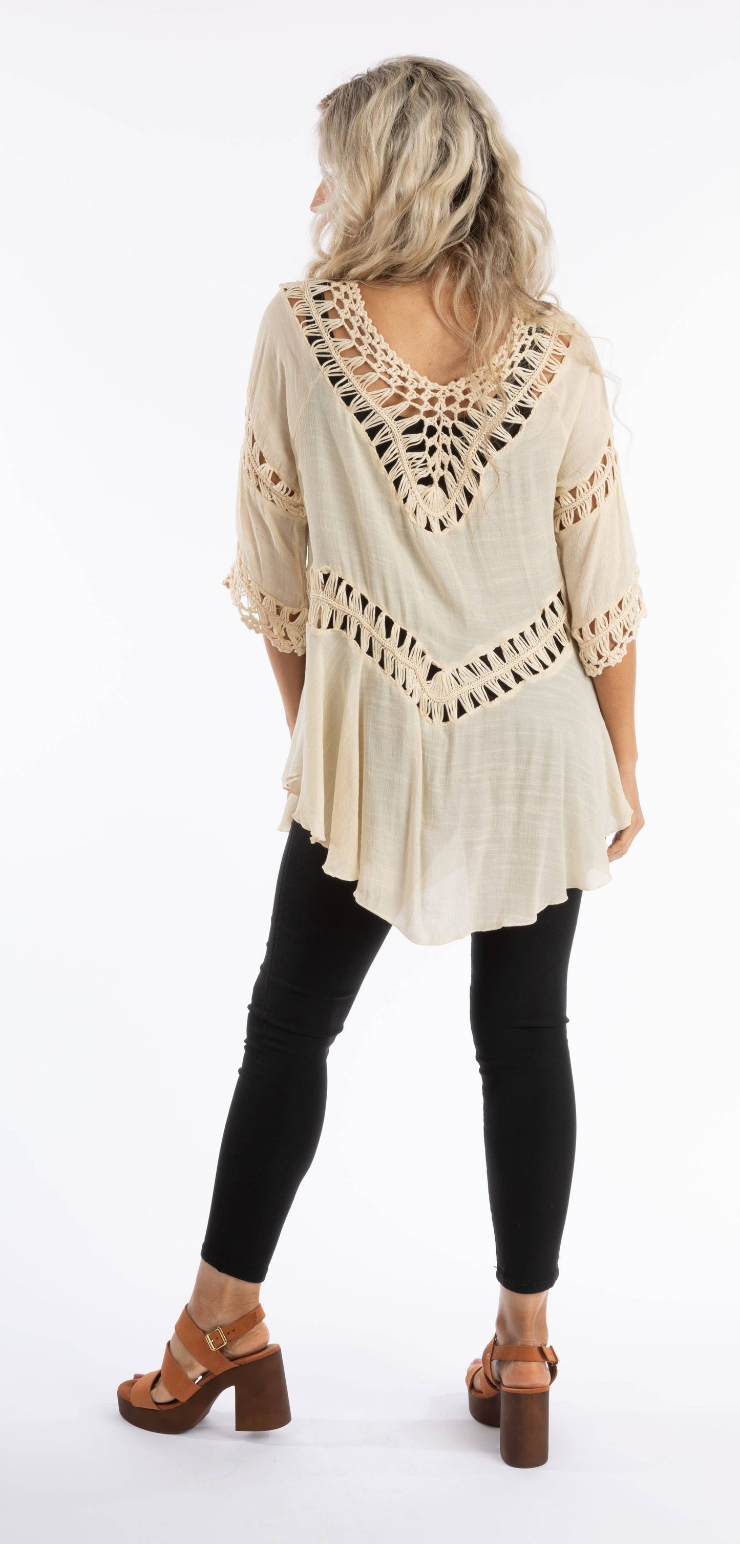 Woman wearing a beige crochet top and black leggings on a white background