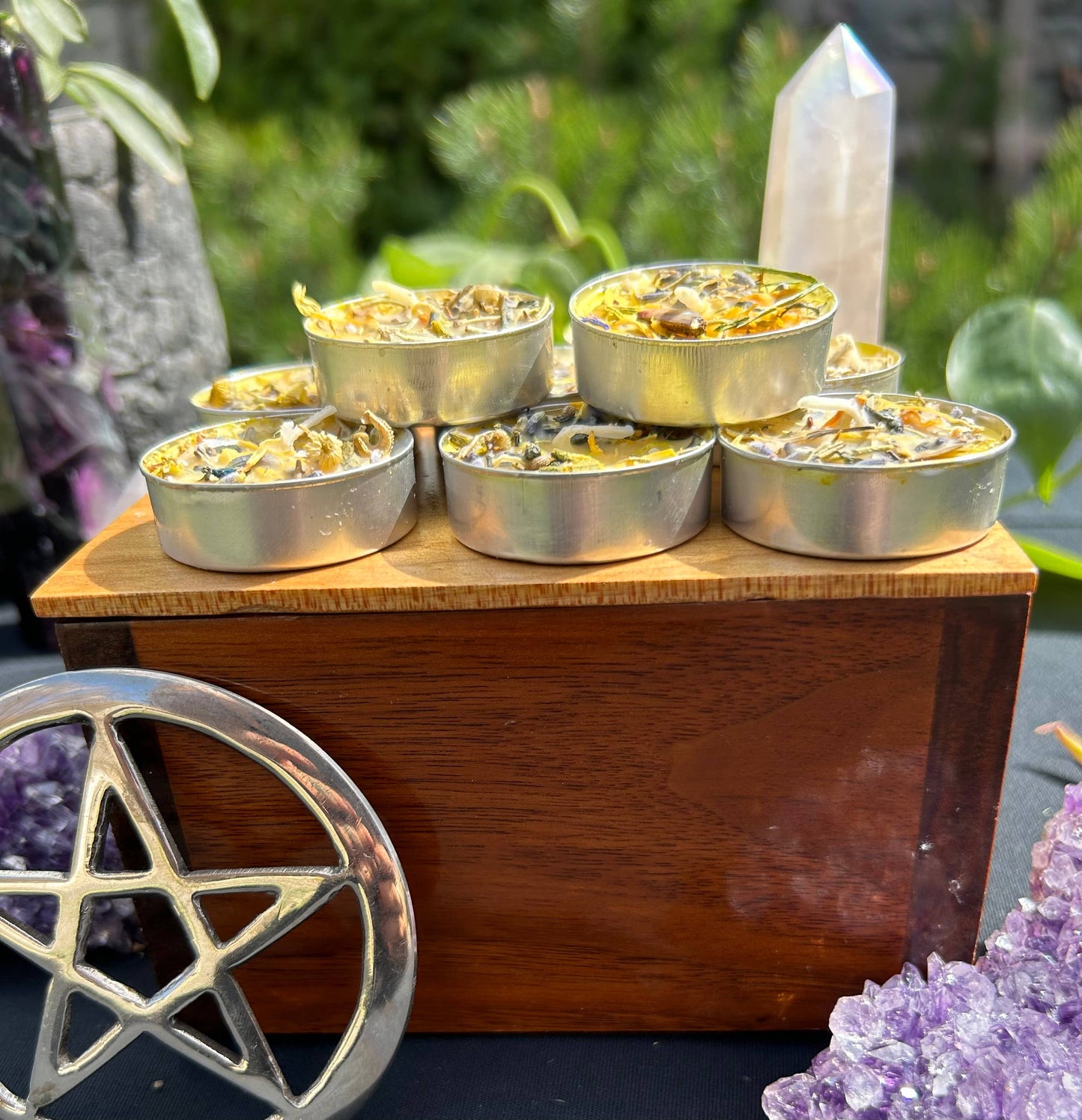 Set of small spell candles in a metallic containers on a wooden stand with crystals and plants in the background