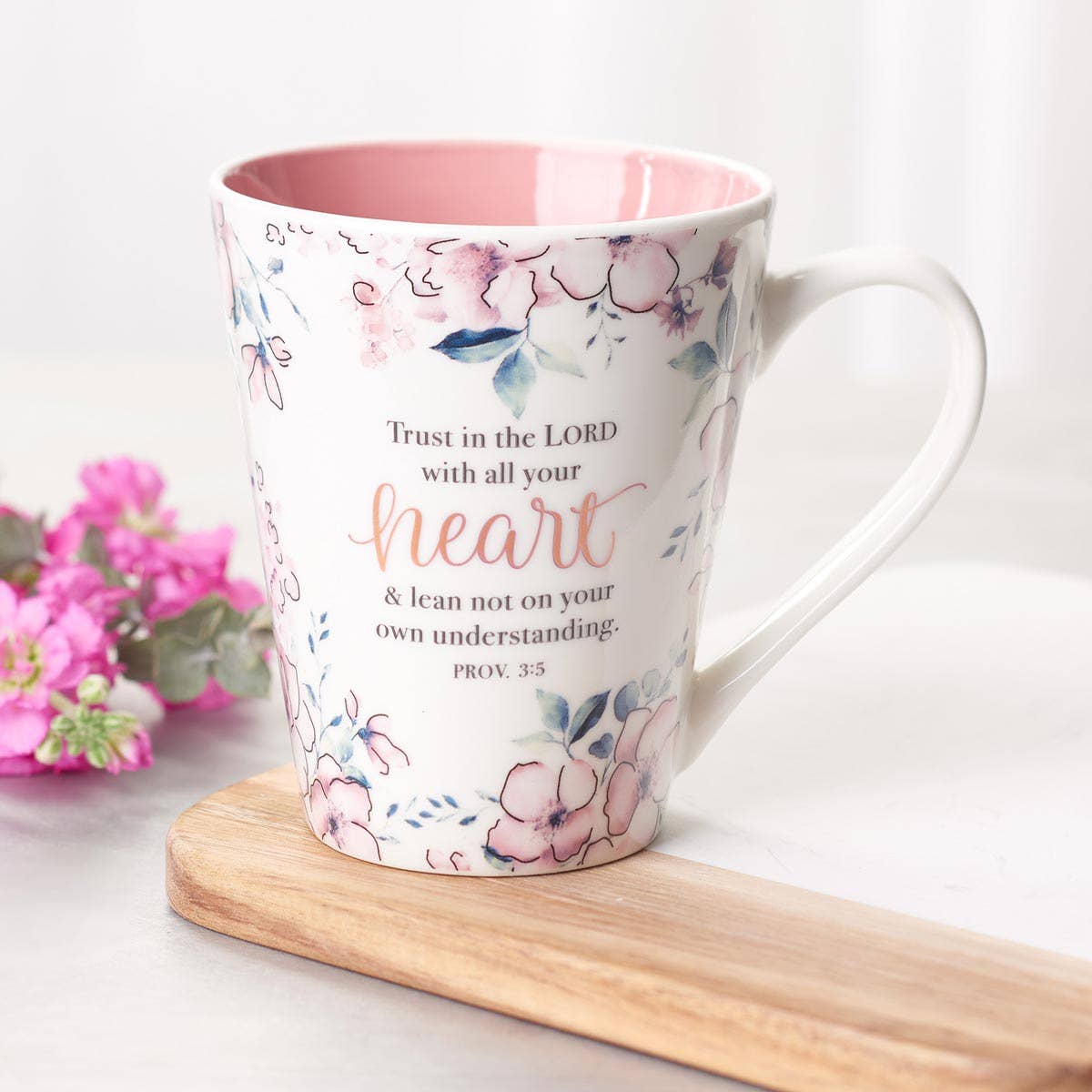 Floral mug with motivational quote on a white surface with flowers in the background