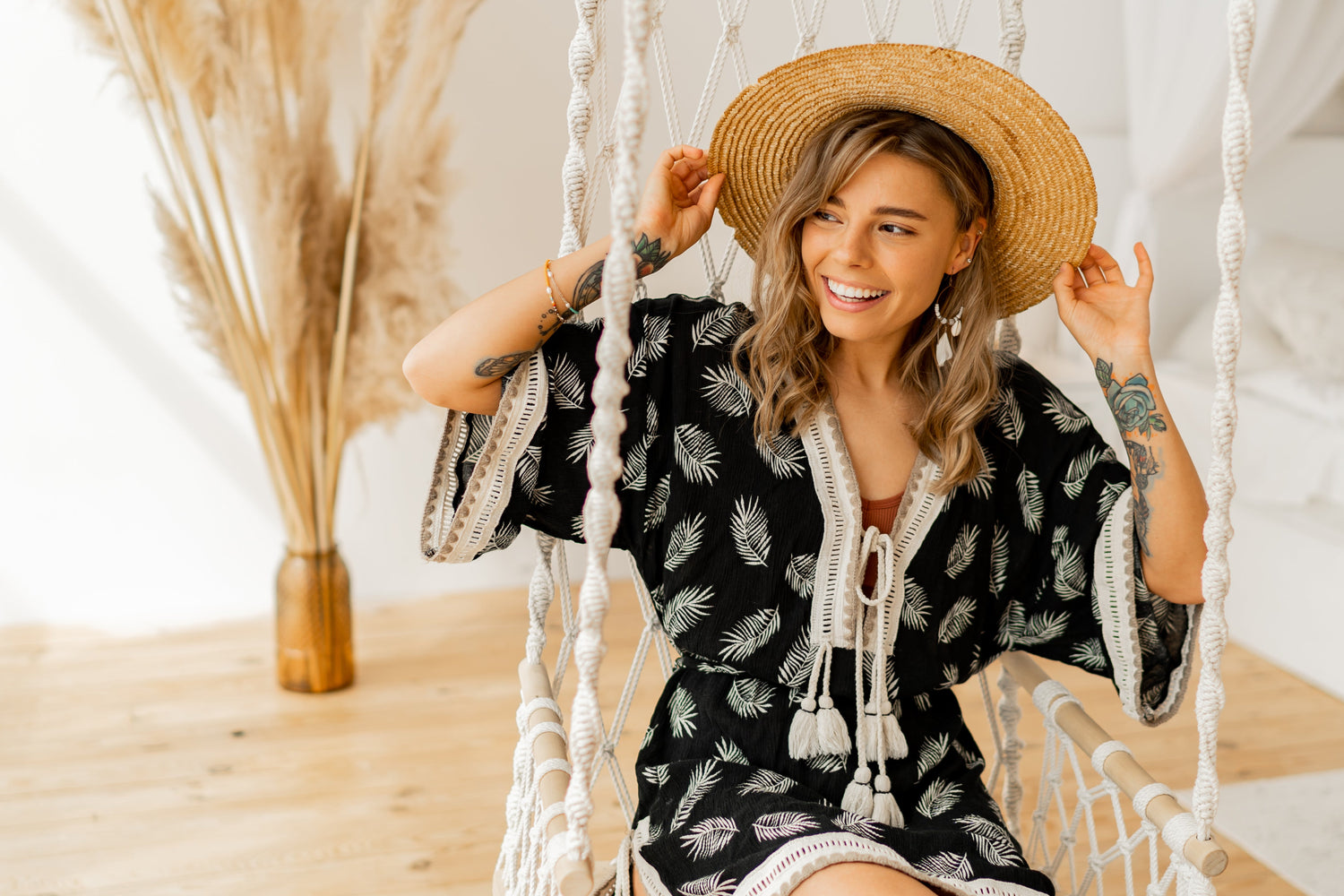Beautiful BOHO lady with straw hat smiling with a black and cream romper dress on swing