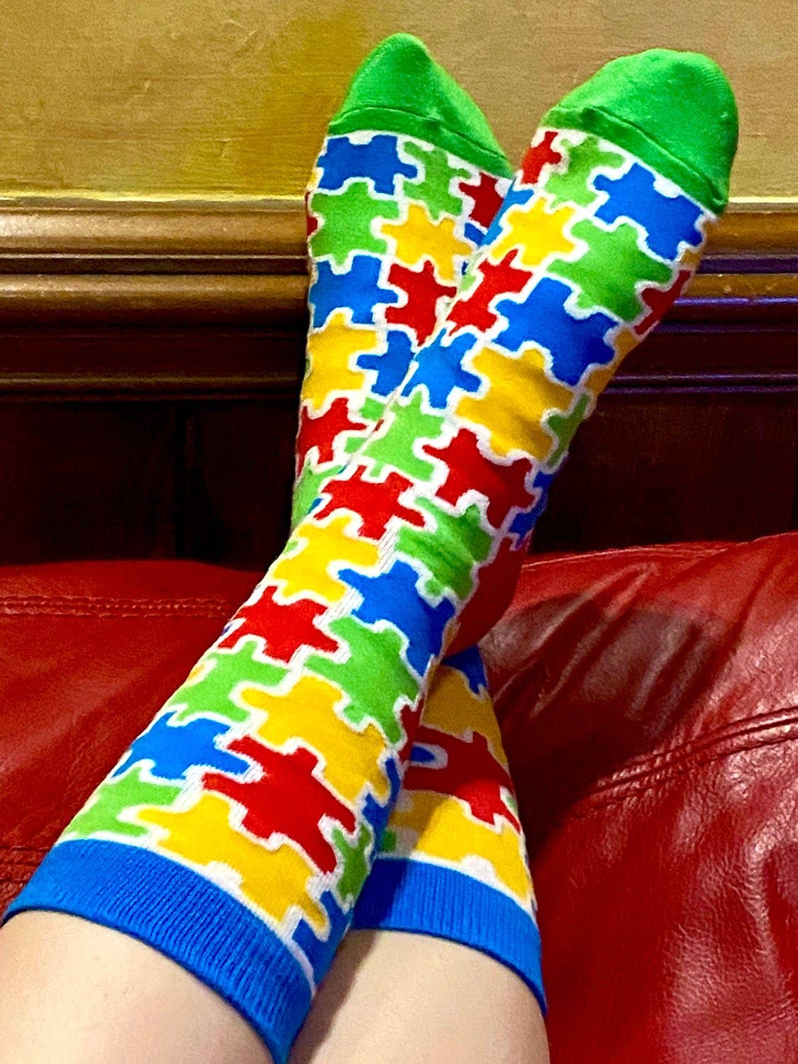 Colorful puzzle-patterned socks on a person sitting on a red couch.