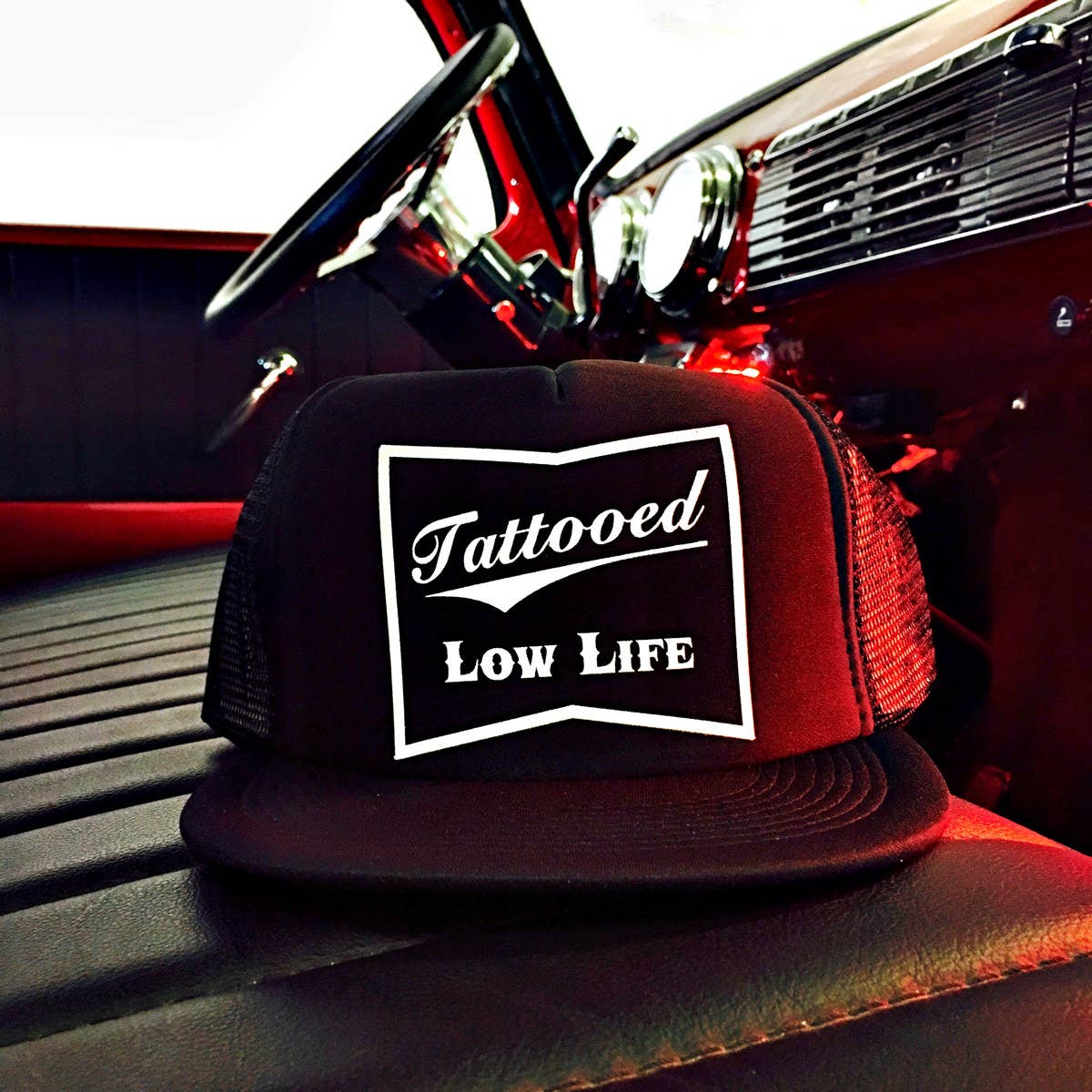 Trucker hat with 'Tattooed Low Life' logo on a car dashboard