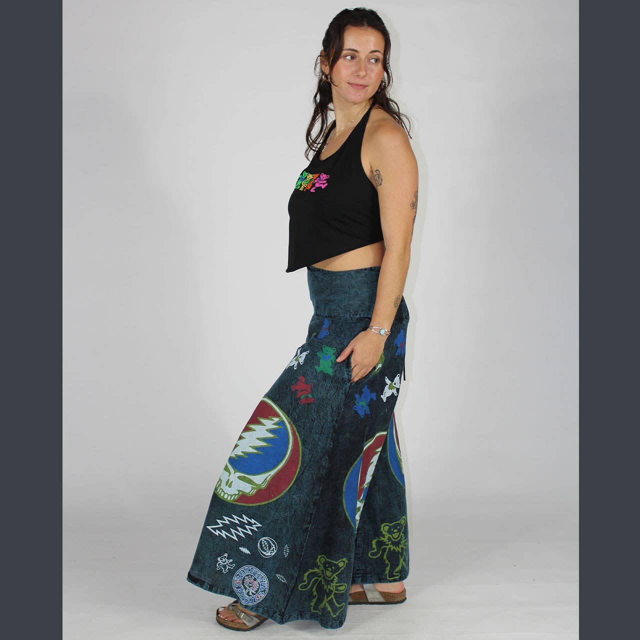 Woman wearing a black top with colorful designs and a patterned blue skirt on a plain background
