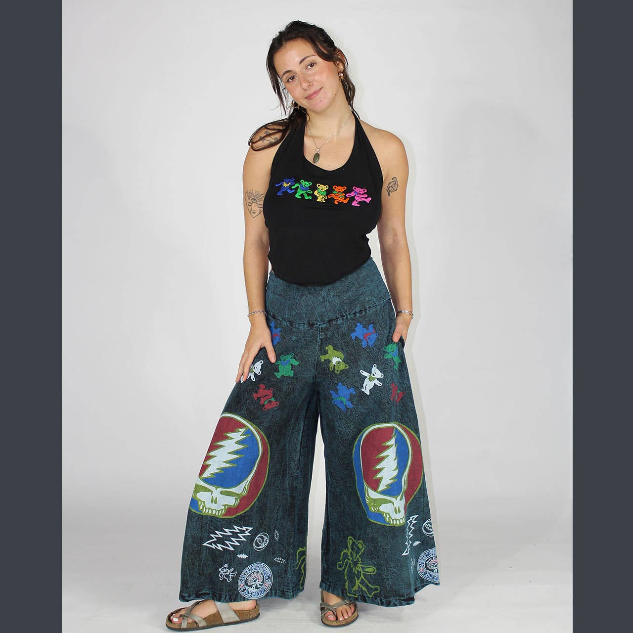 Woman wearing a black tank top with colorful designs and blue pants with Grateful Dead logos on a white background
