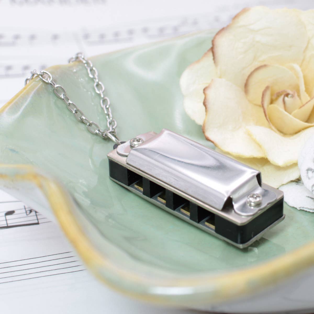 Harmonica necklace on a green dish with a white rose and sheet music in the background