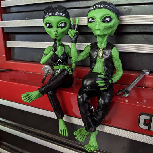 Two green alien figurines sitting on a toolbox with tools around them.