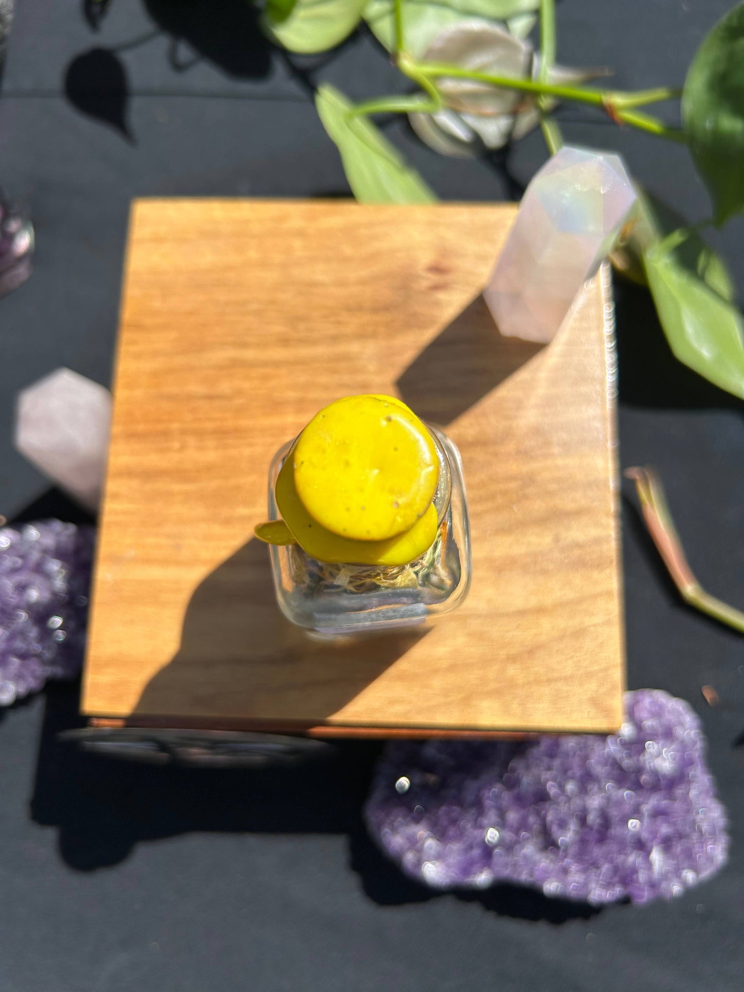 Small glass bottle with yellow cap on a wooden block, surrounded by crystals and plants