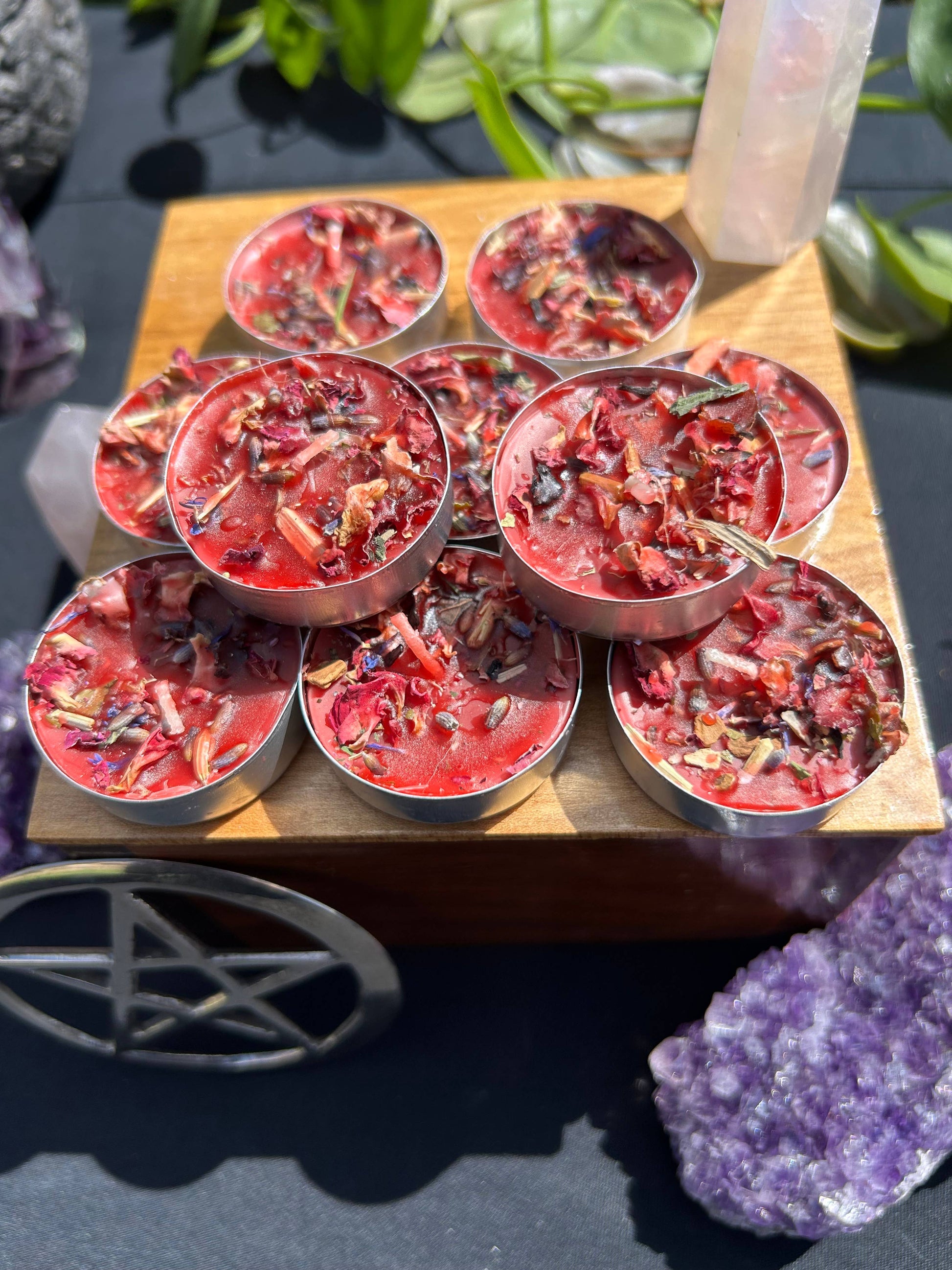 Red wax melts in metal containers on a wooden board with crystals and a pentacle symbol in the background.