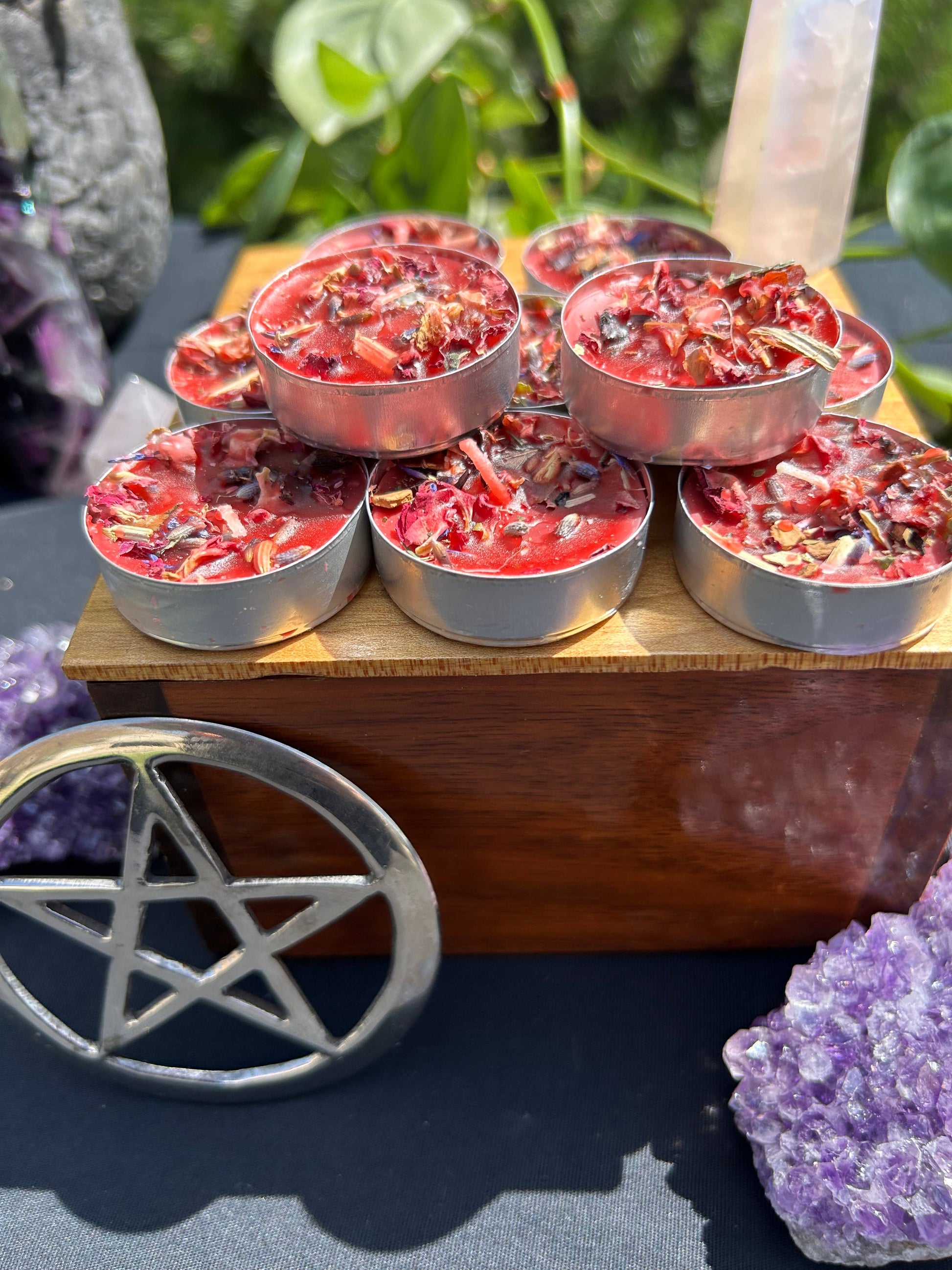 Small candles in metal containers on a wooden stand with crystals and a pentacle symbol in the foreground.