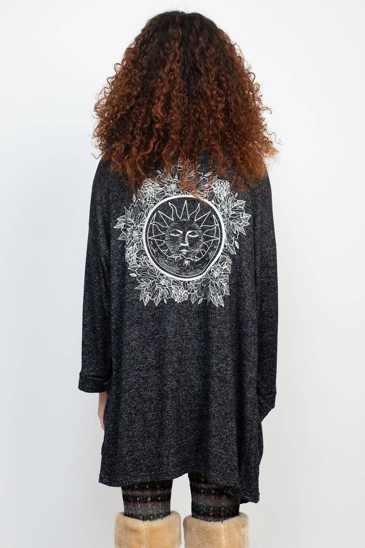 Person wearing a black cardigan with a white mandala design on the back, standing against a white background.