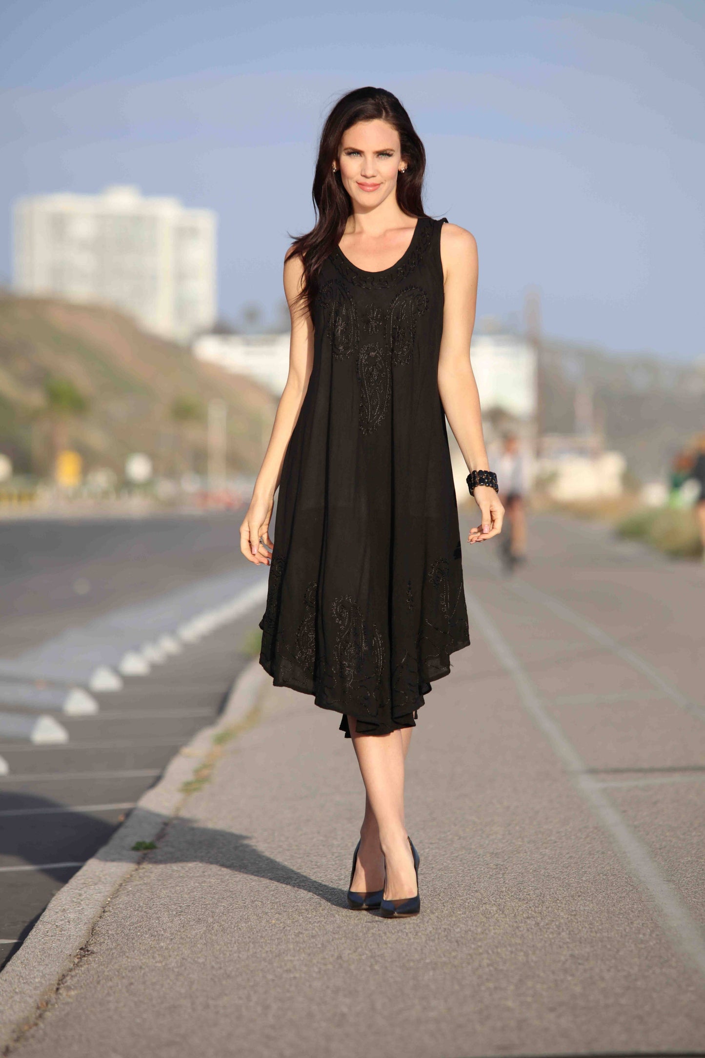 Woman in a black dress walking on a road with buildings in the background