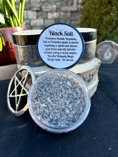 Container of black salt with a label and pentacle symbol on a dark surface.