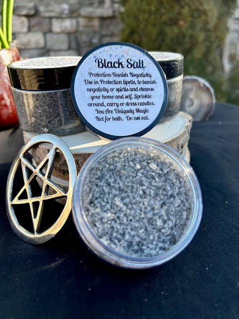 Container of black salt with a pentagram symbol and descriptive label on a dark surface.