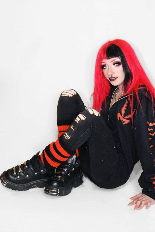 Person with red hair and black outfit sitting on a white background