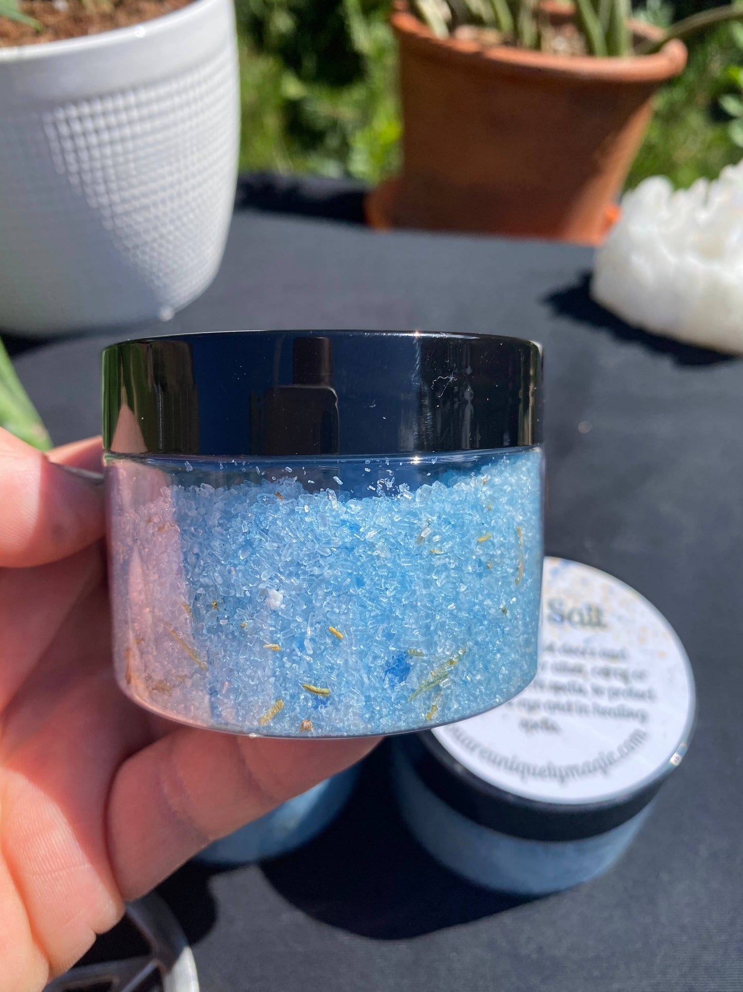 Hand holding a small container of blue glitter with a blurred outdoor background