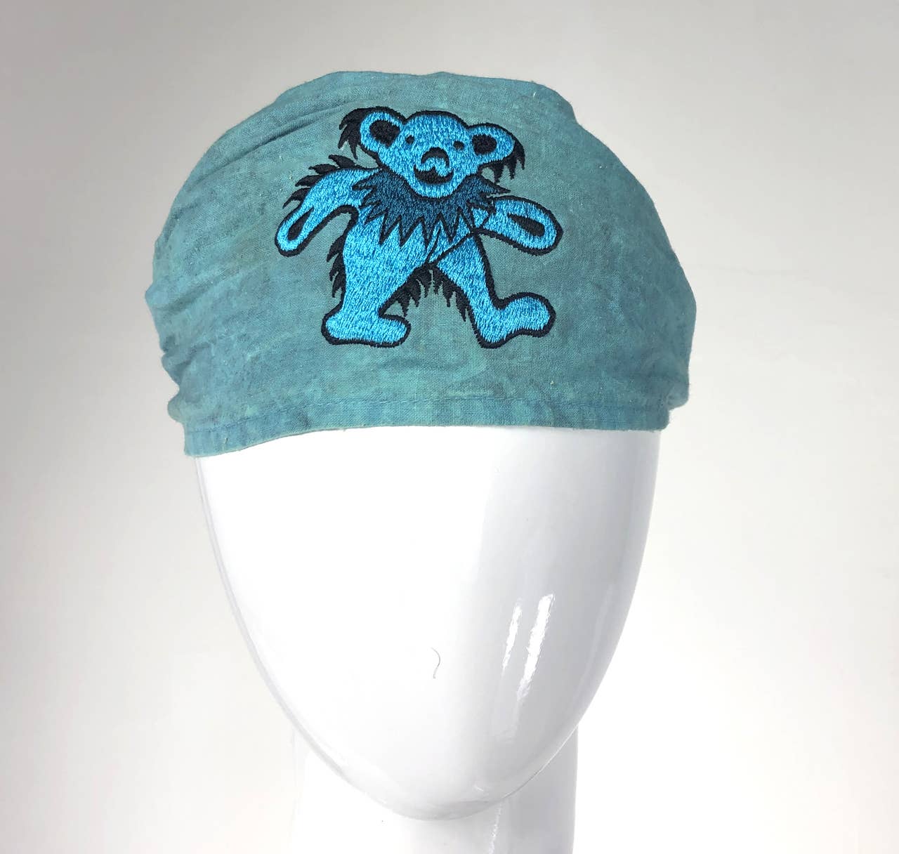 Blue headband with a bear design on a mannequin head against a white background
