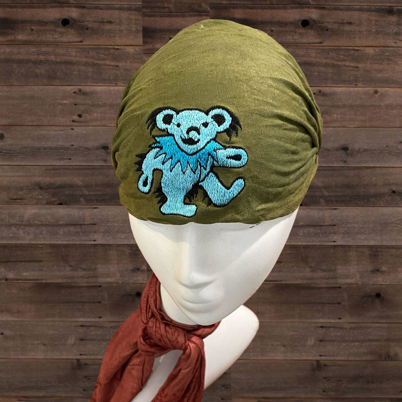 Green headscarf with blue bear patch on a mannequin against a wooden background