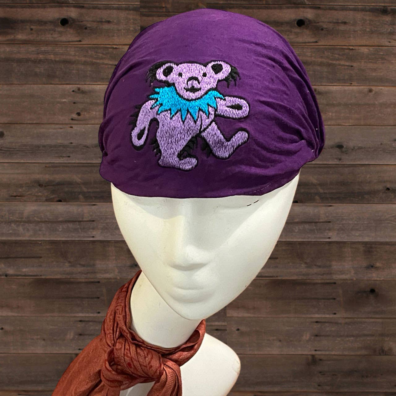 Purple headscarf with a colorful bear design on a mannequin against a wooden background
