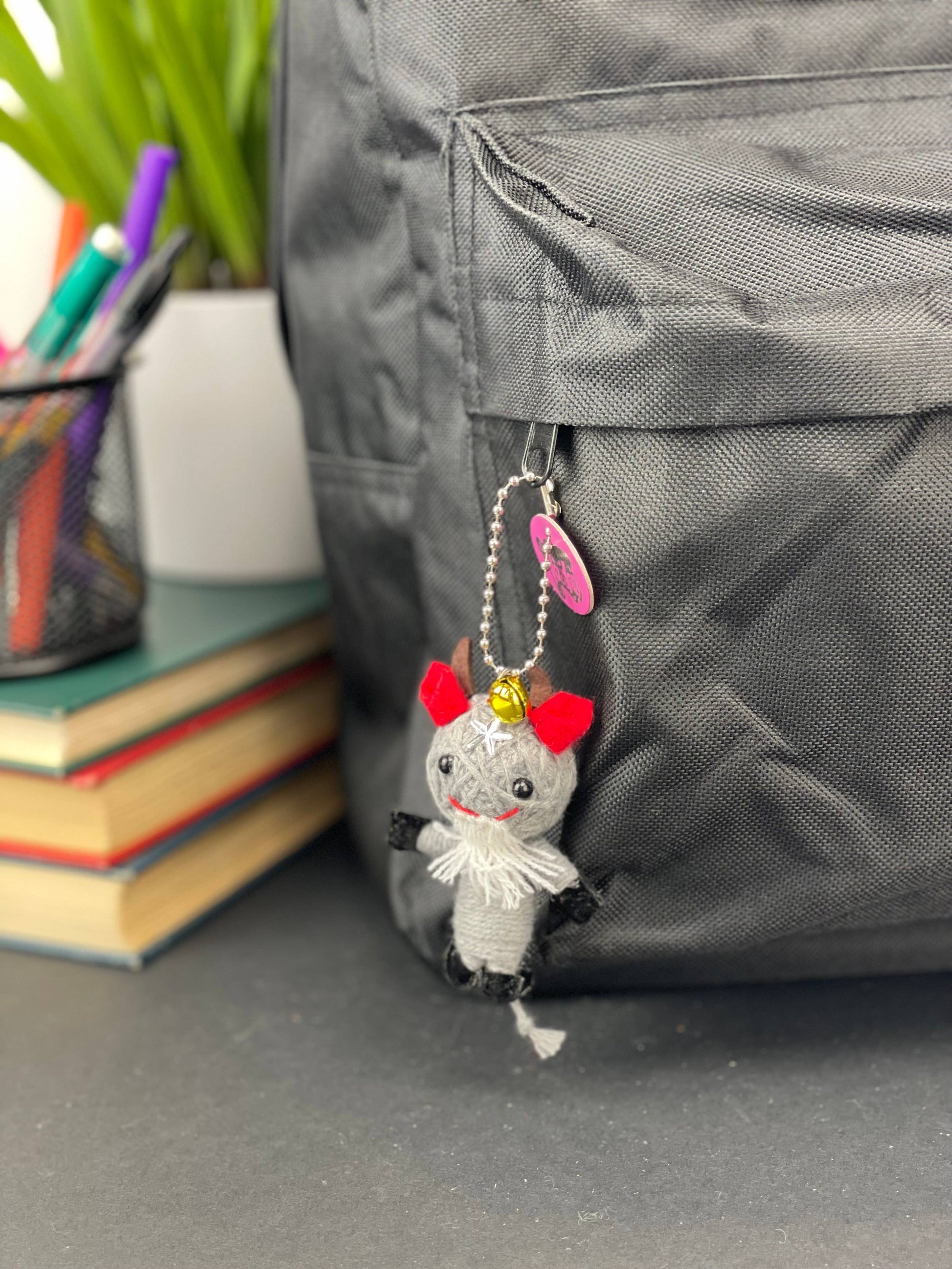 Small plush keychain attached to a backpack with stationery items in the background