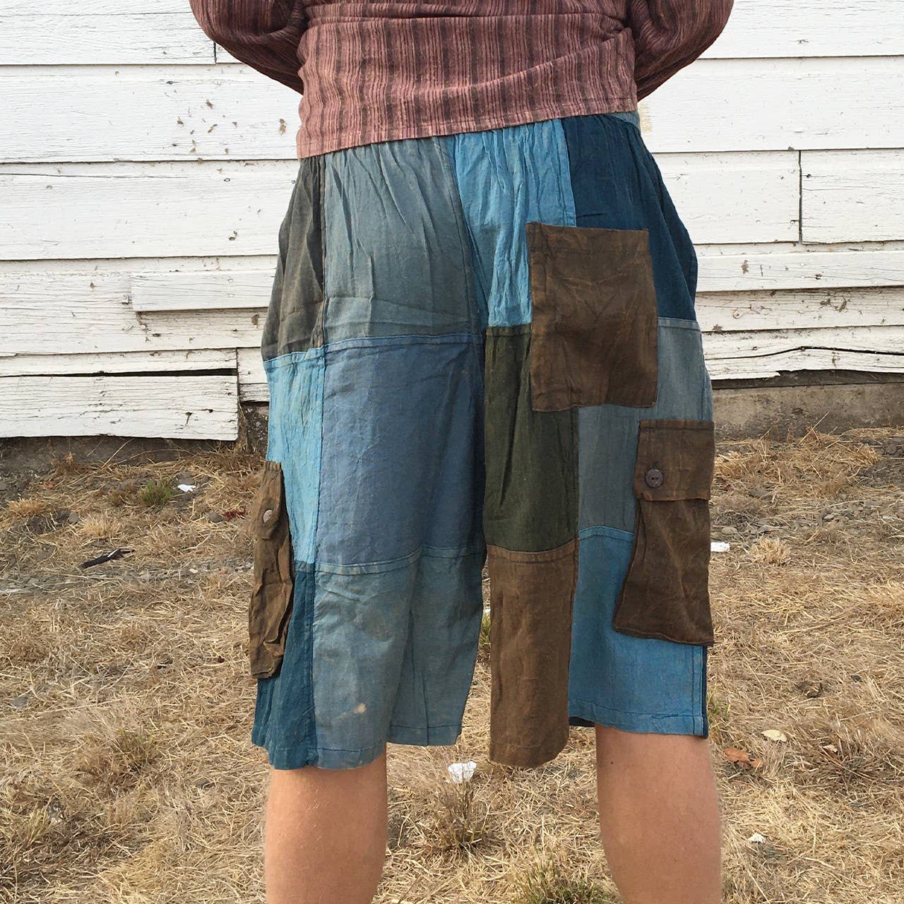 Person wearing a patchwork shorts with blue, brown, and green colors against a wooden wall.