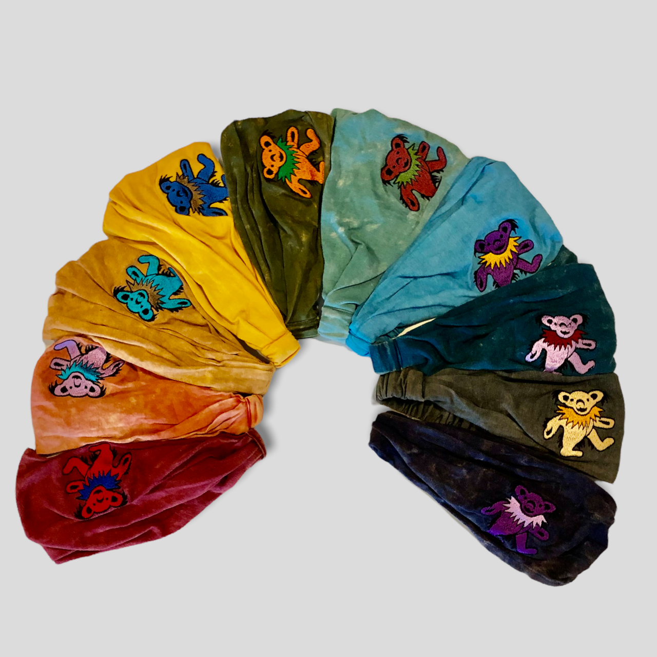 Colorful velvet scrunchies with embroidered designs arranged in a circular pattern on a light gray background.