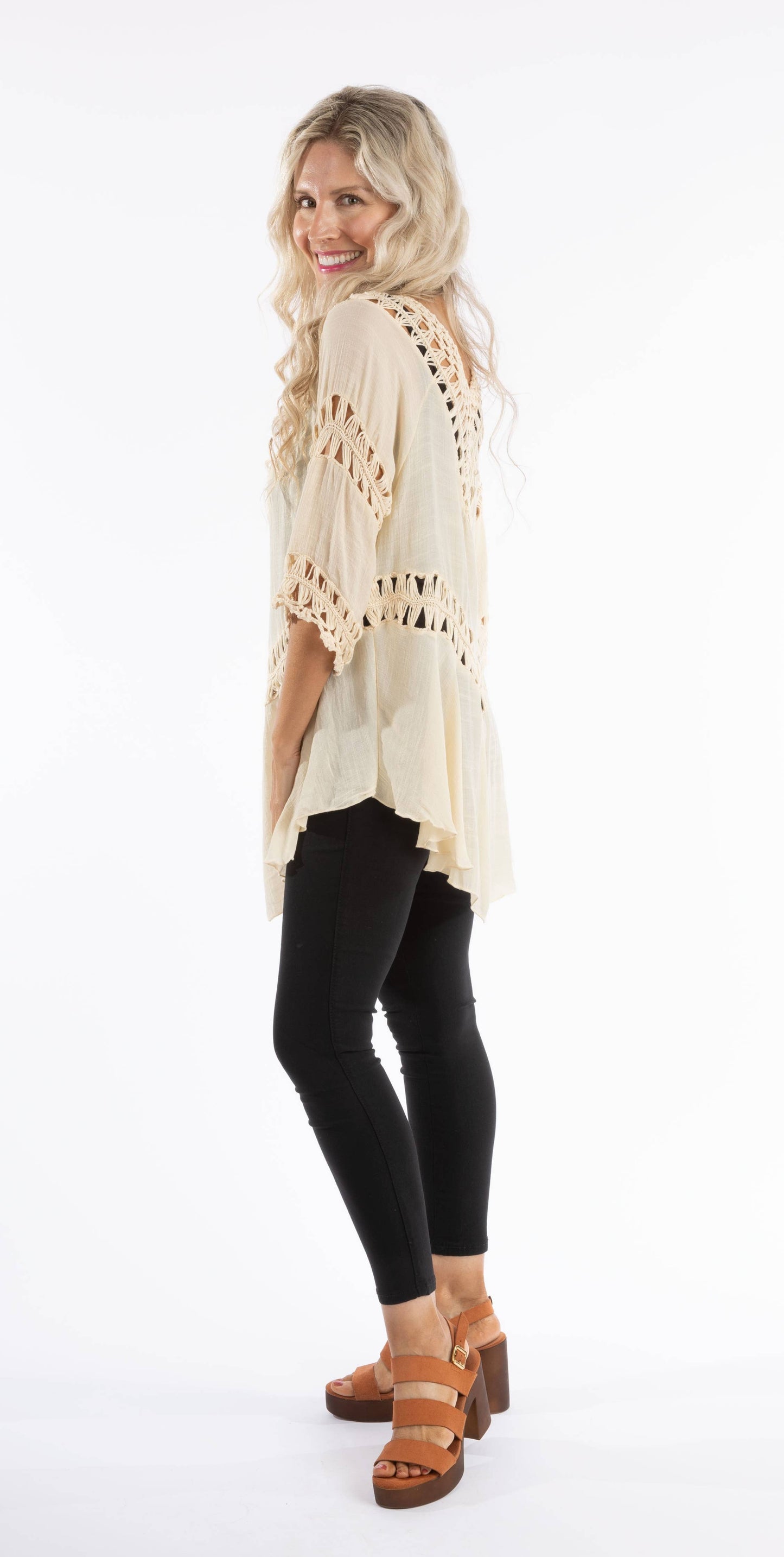 Woman wearing a beige lace top, black leggings, and brown sandals on a white background