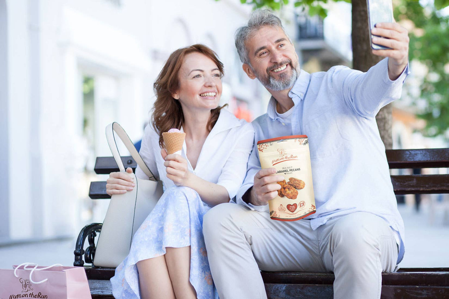 Man and woman sitting on a bench, eating ice cream and holding a bag of cookies.