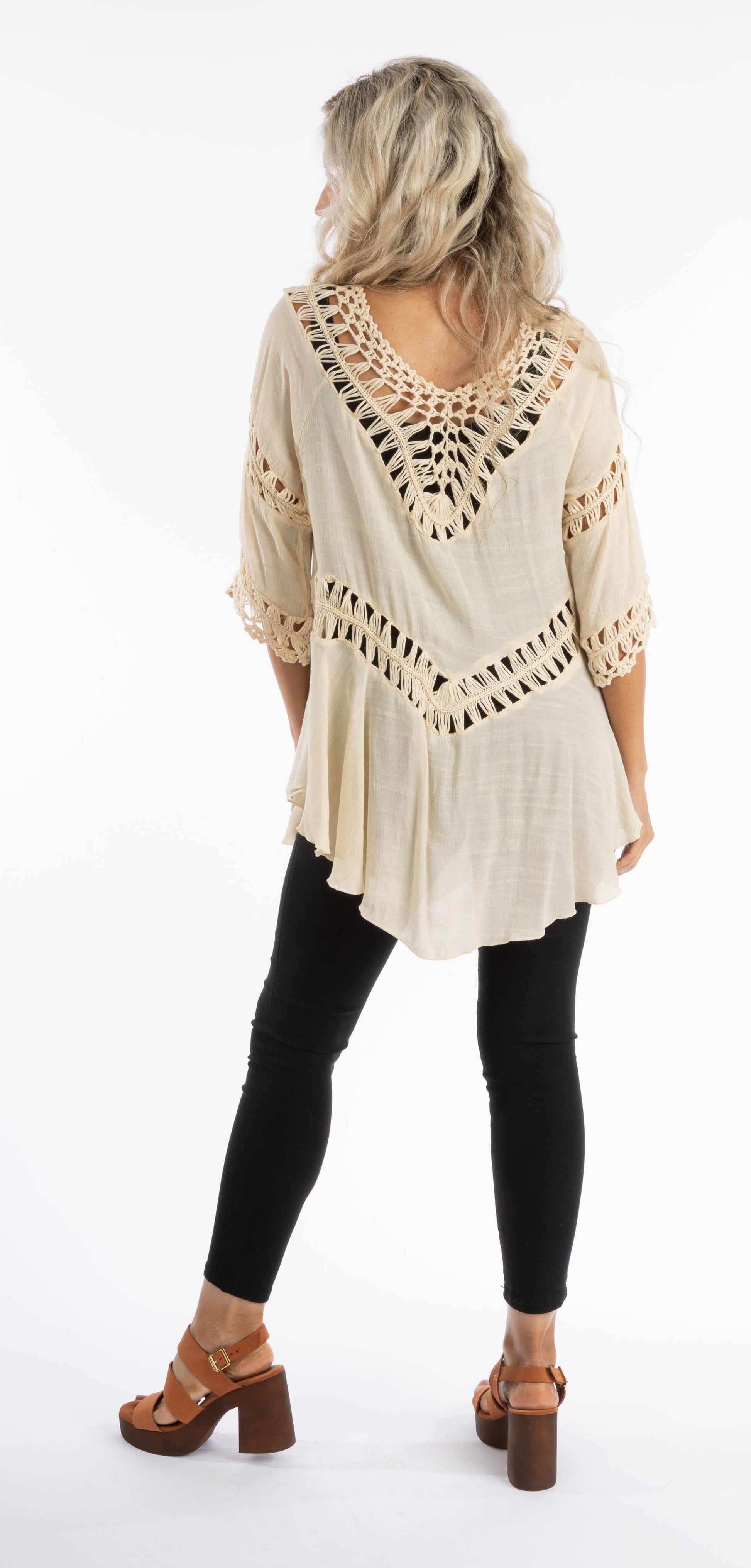 Woman wearing a beige crochet top and black leggings on a white background