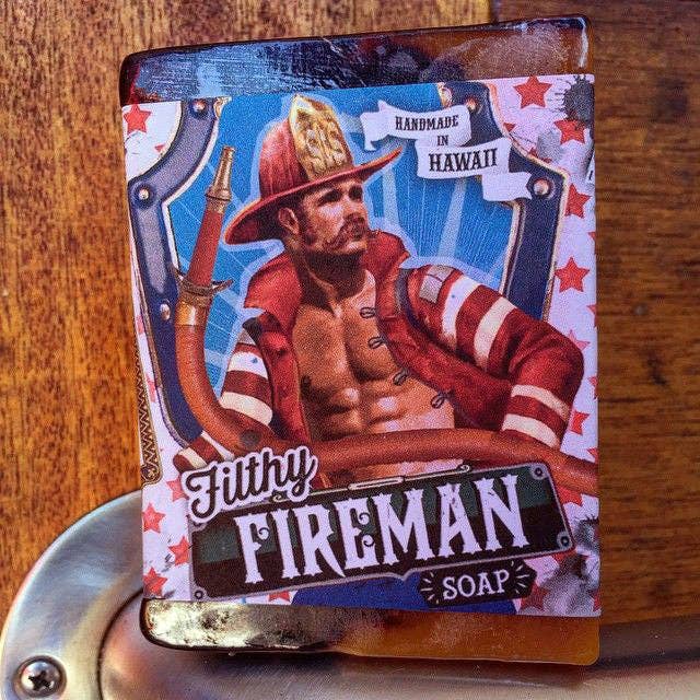 Soap packaging featuring a firefighter design with 'Filthy Fireman Soap' text on a wooden surface.