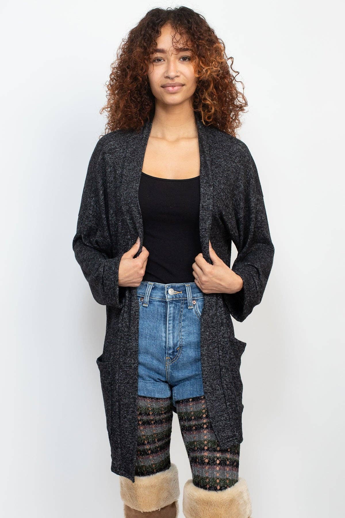 Woman wearing a long dark cardigan over a black top and blue jeans on a white background