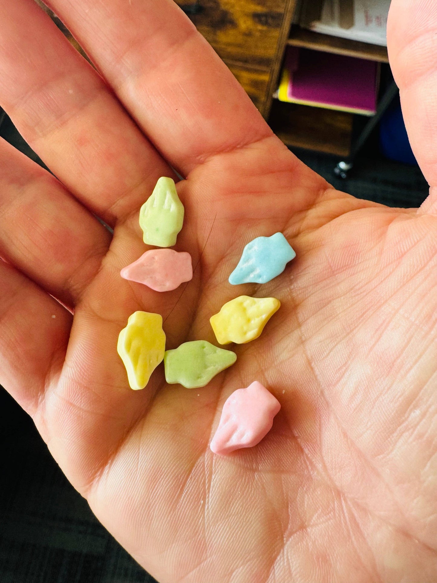 Colorful candy shaped like leaves held in a hand with a blurred indoor background