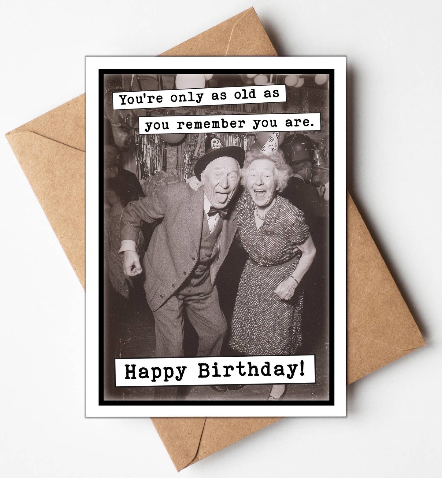Birthday card with vintage photo of an elderly couple and humorous text, placed on a brown envelope.