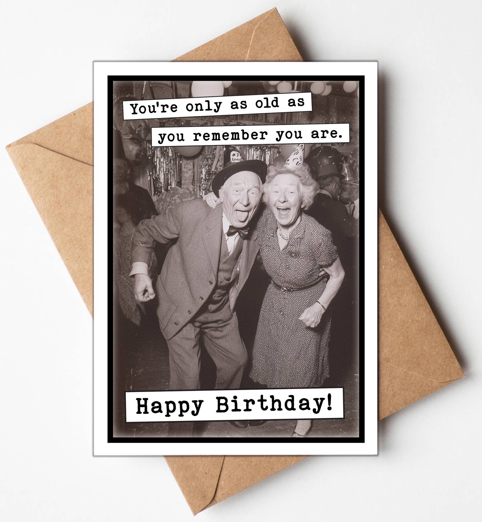 Birthday card with vintage photo of an elderly couple and humorous text, placed on a brown envelope.