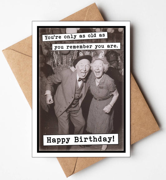 Birthday card with vintage photo of an elderly couple and humorous text, placed on a brown envelope.
