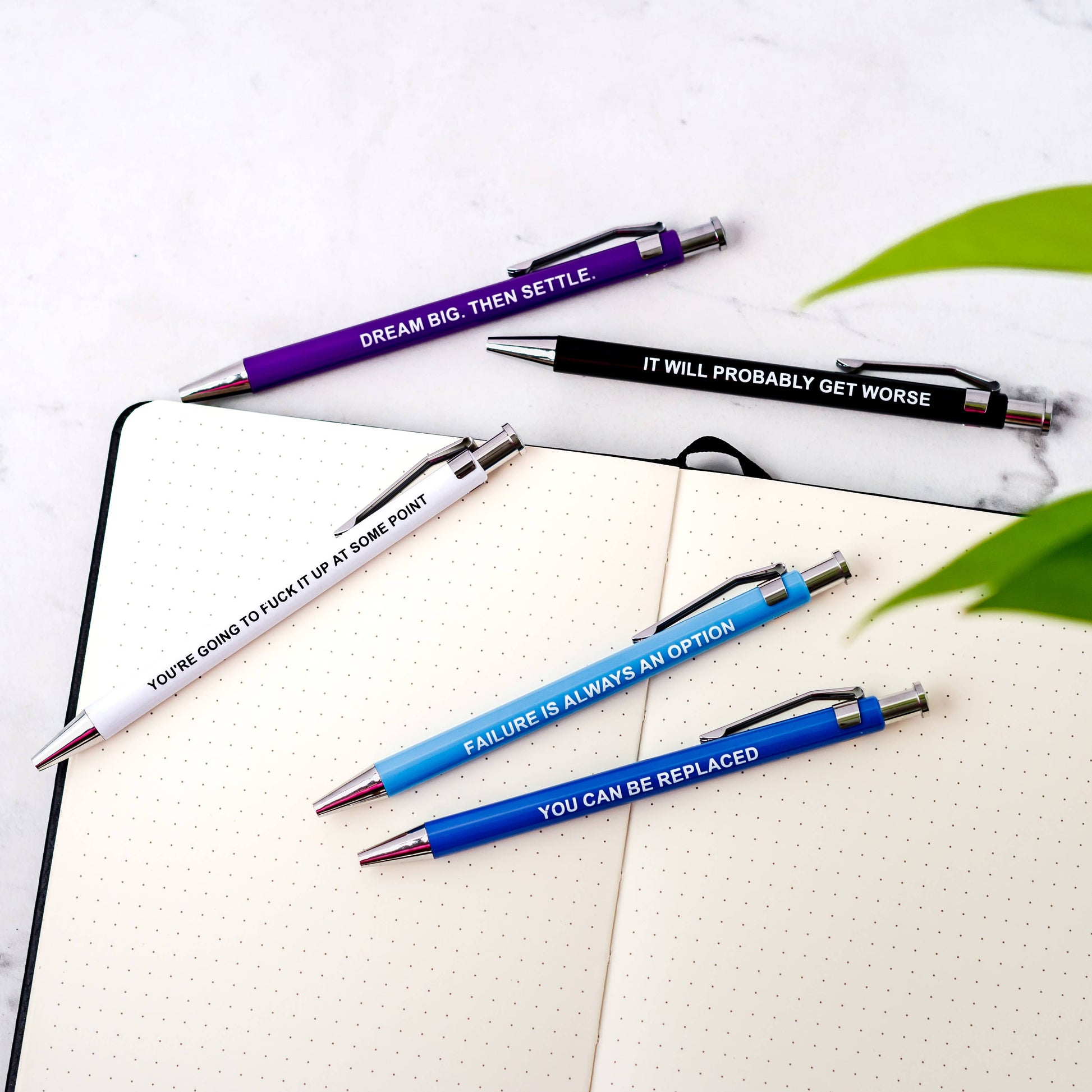 Four pens with motivational quotes on a notebook with a white background