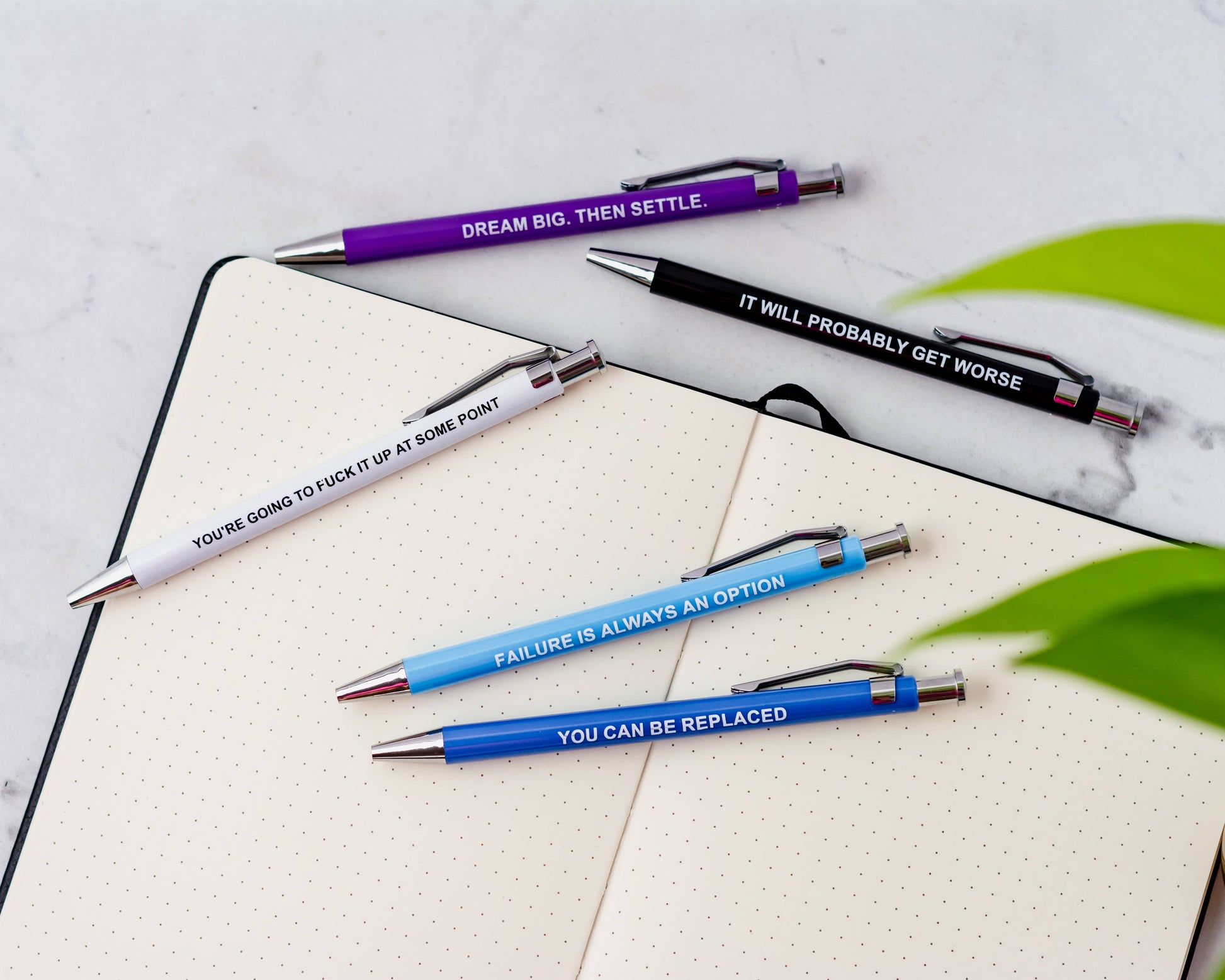 Five motivational pens on a notebook with various phrases.