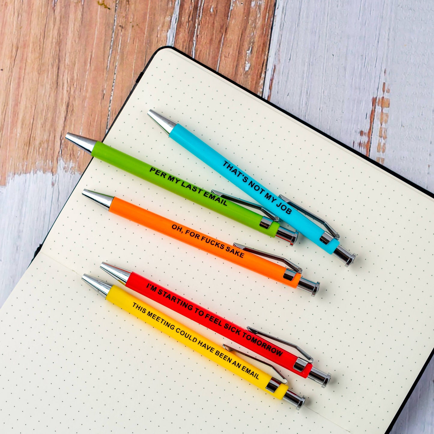 Four colorful pens with humorous text on a notebook