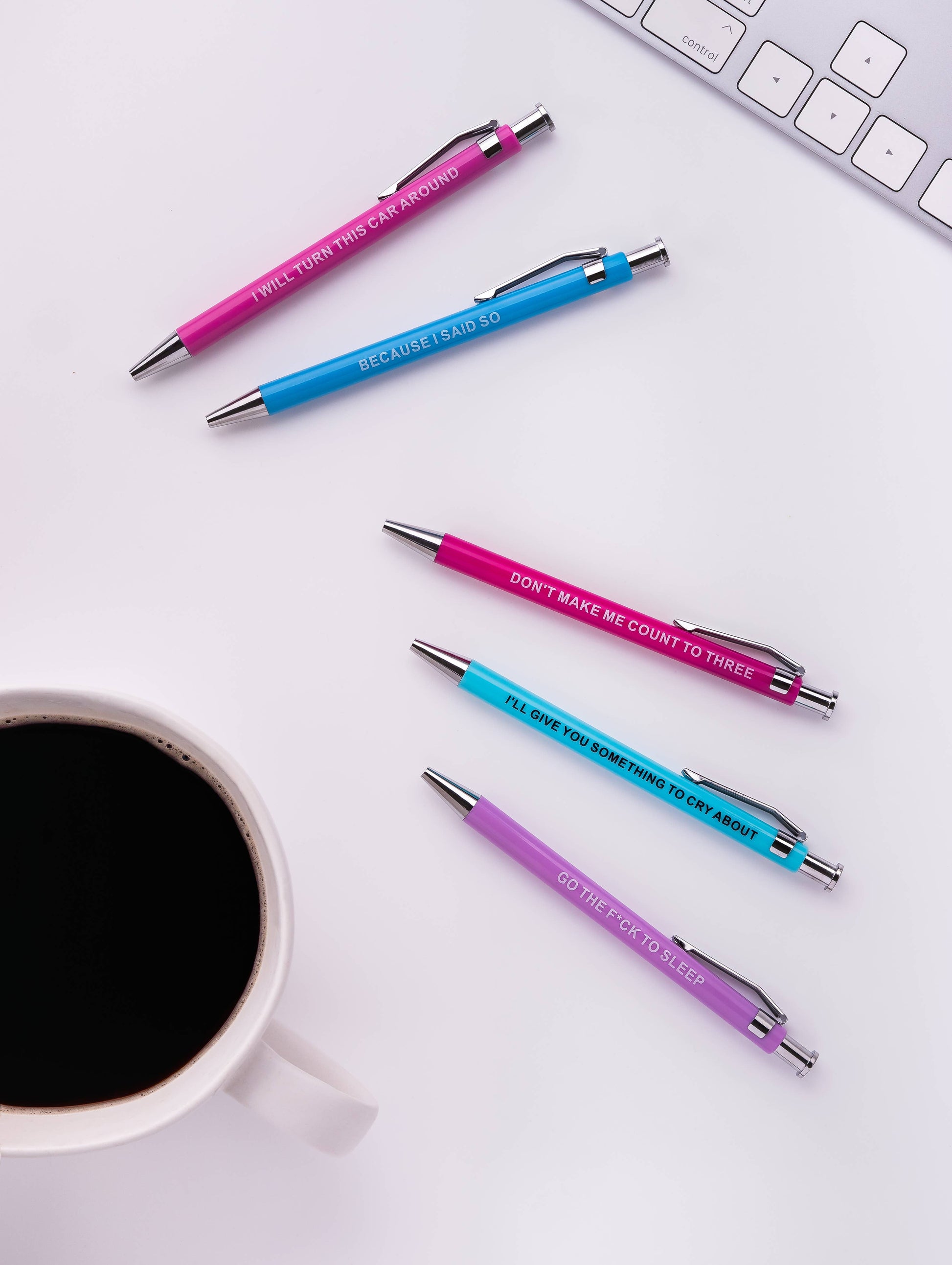 Five promotional pens on a white surface with a cup of coffee and keyboard.