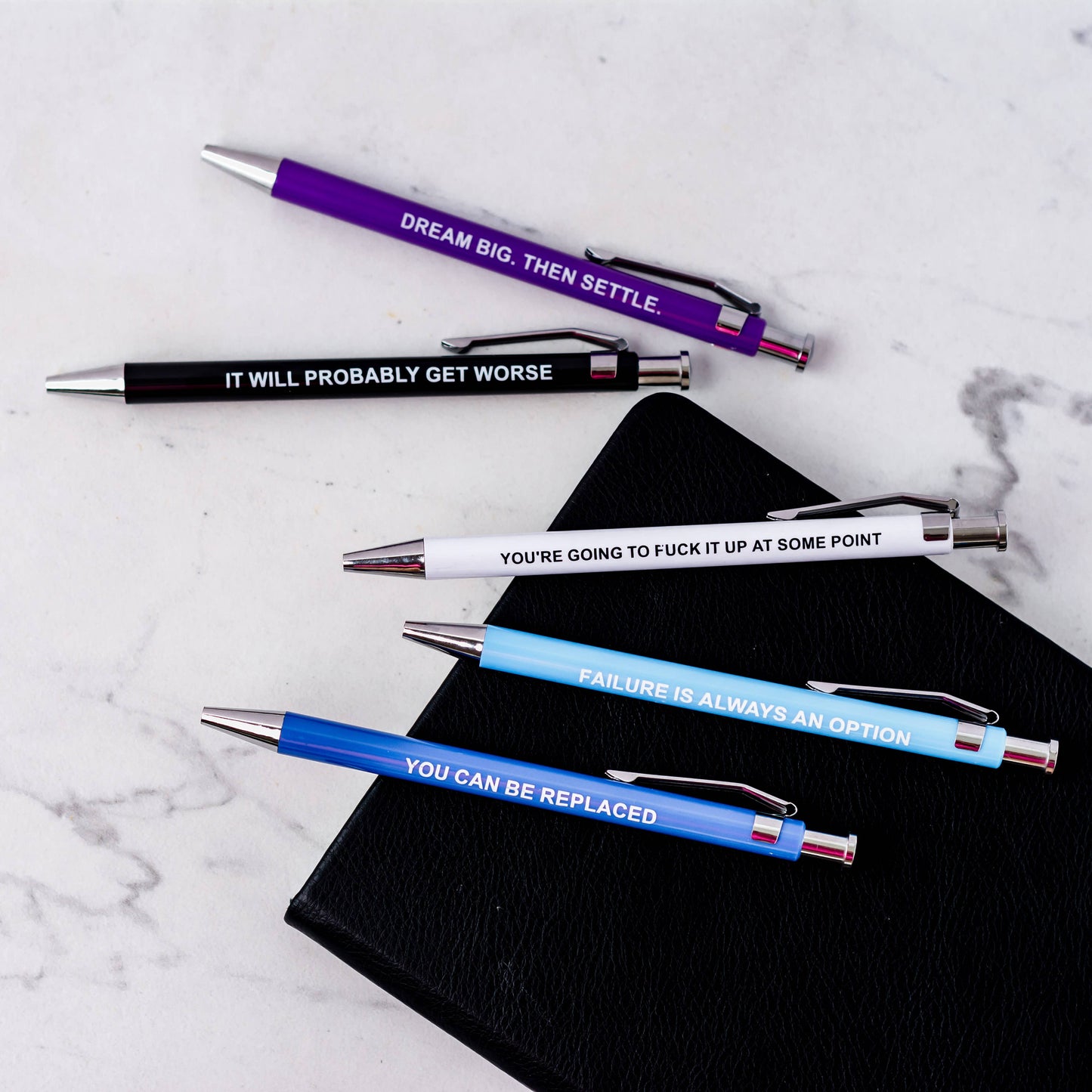 Five pens with motivational quotes on a marble surface