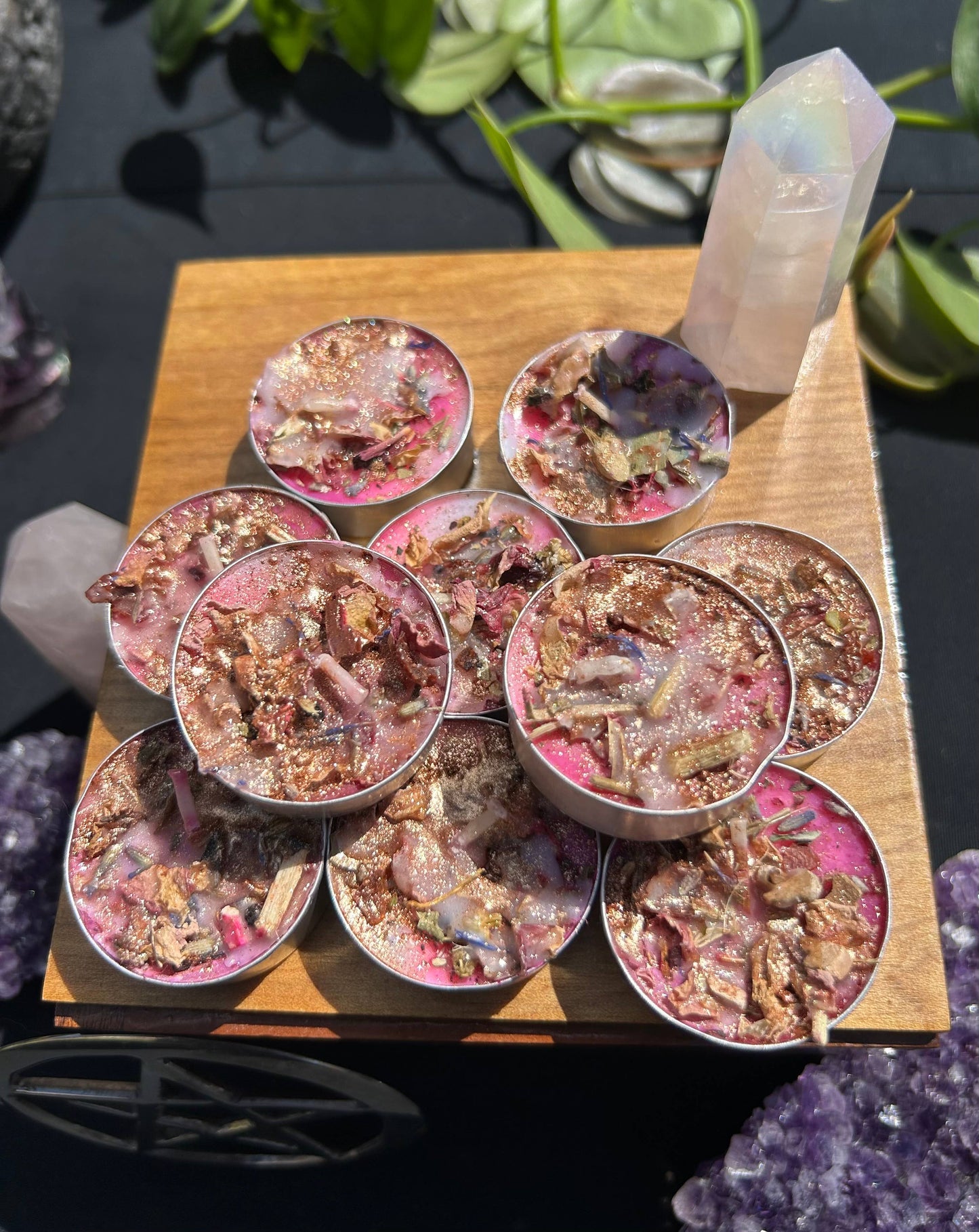 Set of small containers with decorative contents on a wooden board, surrounded by crystals and plants.