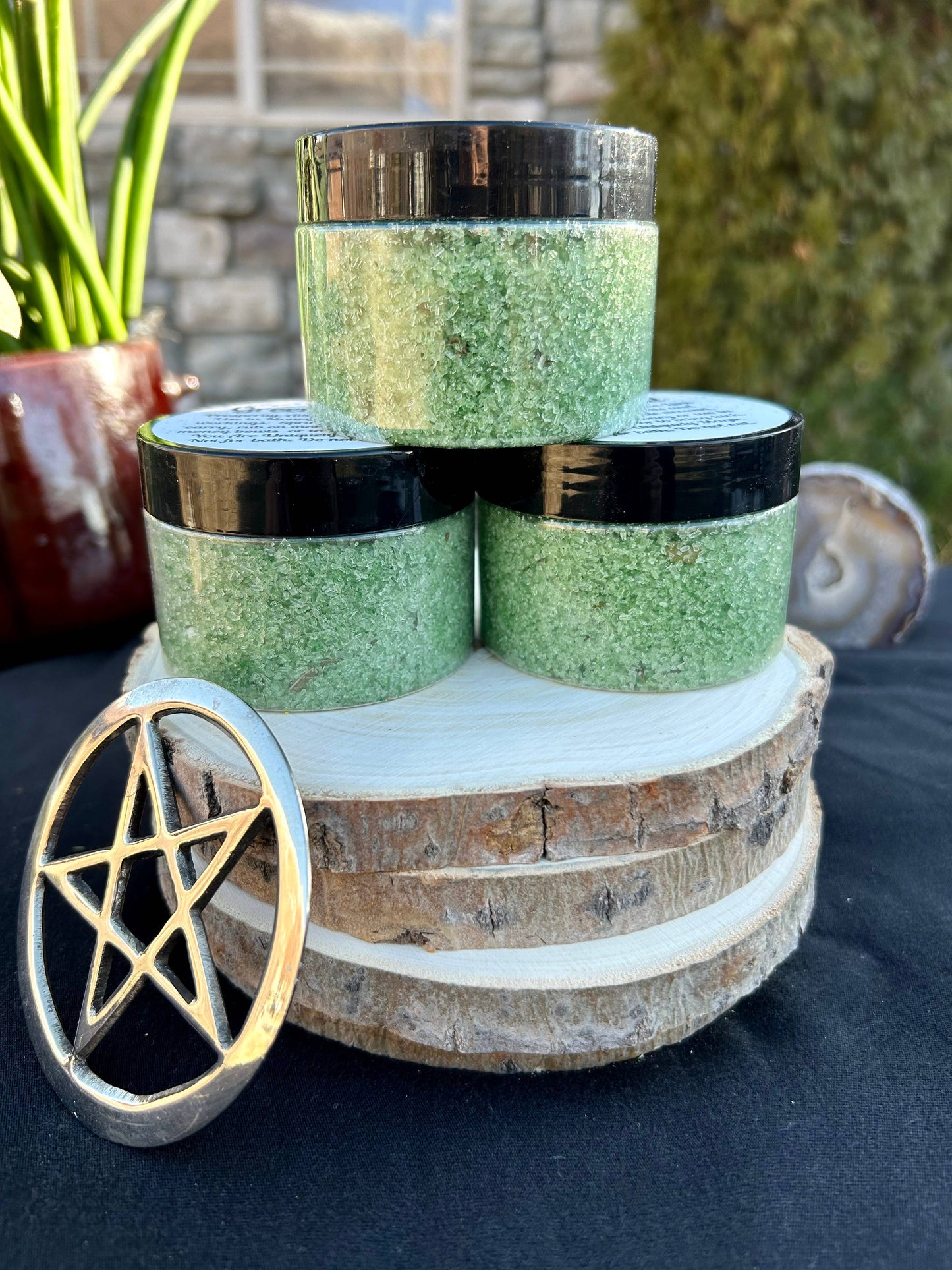 Three green jars with black lids stacked on a wooden block, with a pentacle symbol in the foreground.