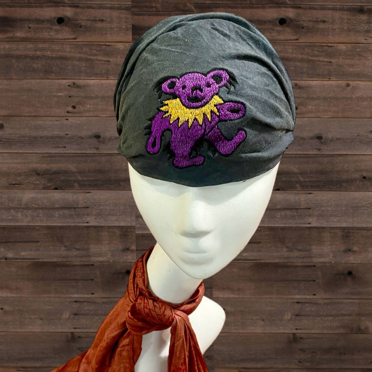 Gray turban with a purple embroidered bear design on a mannequin head against a wooden background