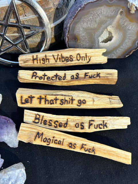 Wooden sticks with profane text on a dark surface with crystals and a pentacle symbol.