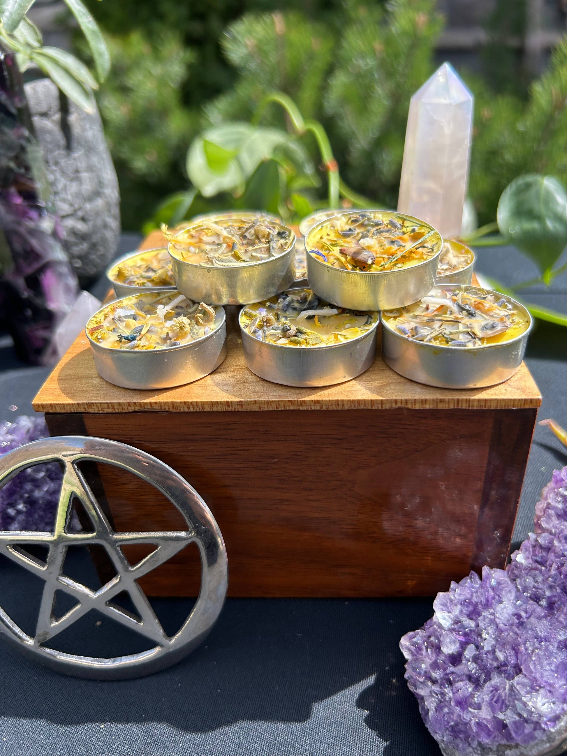 Small metal containers on a wooden block with crystals and a pentacle symbol in the background.
