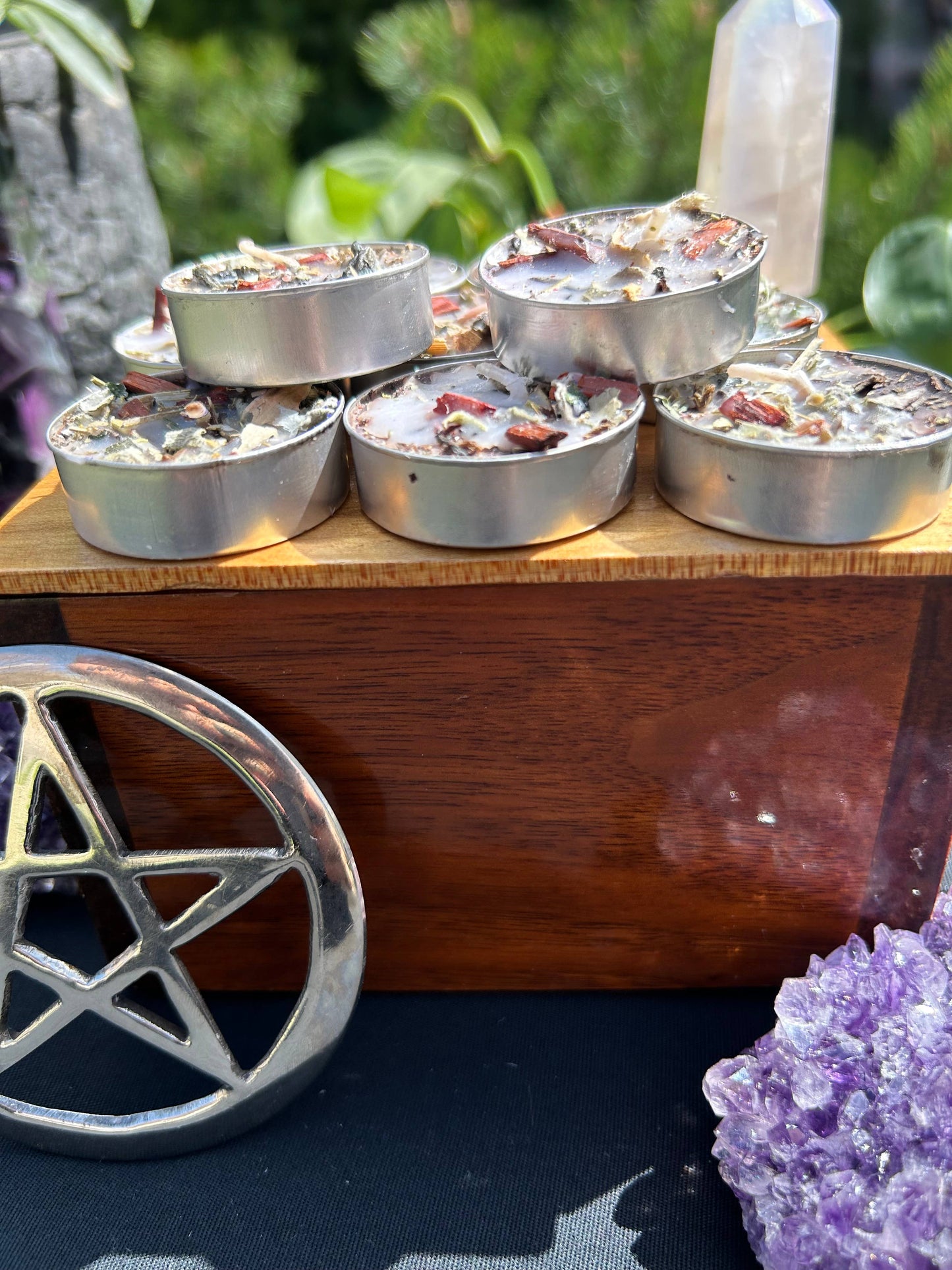 Small metal containers with incense or similar material on a wooden stand, with a pentacle symbol and amethyst crystal in the foreground.