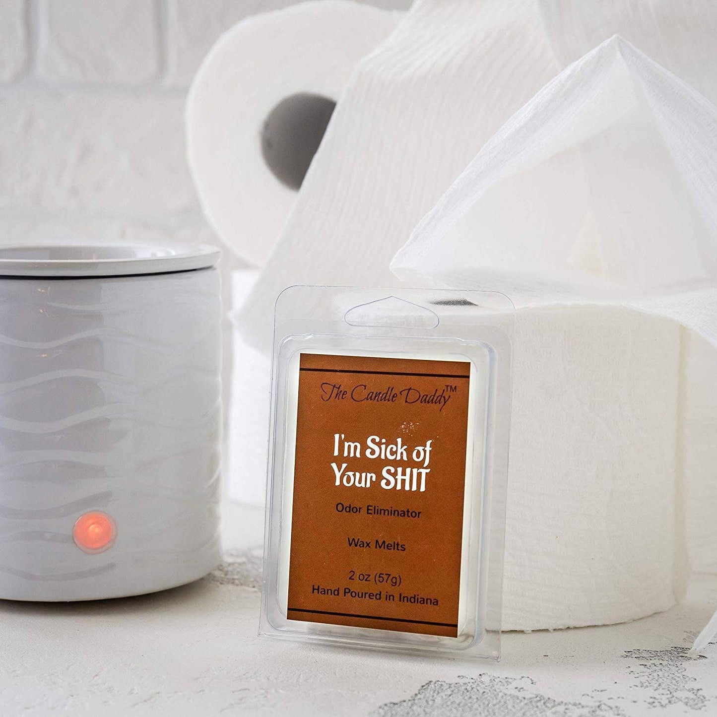Wax melt package labeled 'I'm Sick of Your Shit' next to a wax warmer on a white surface.