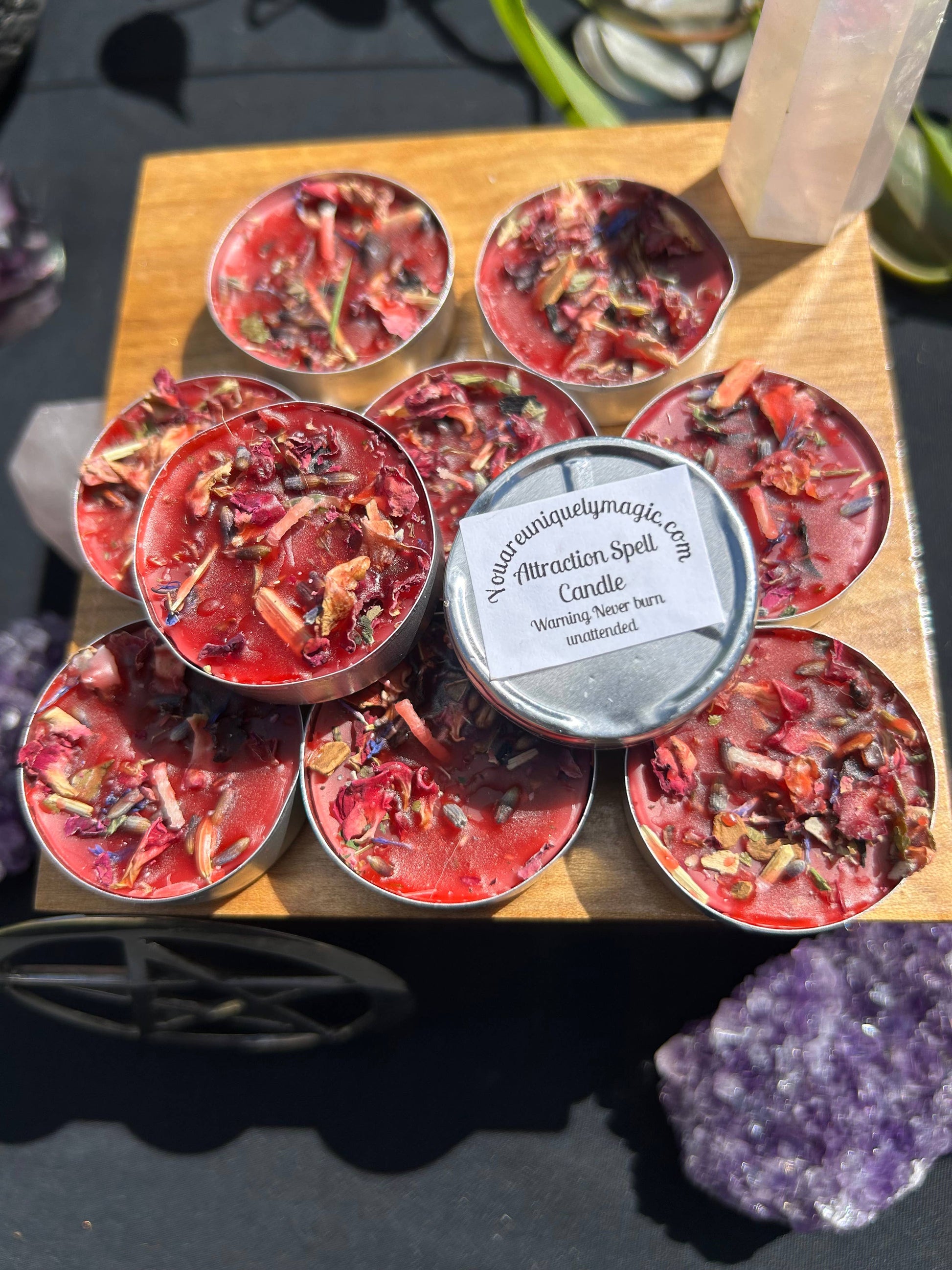 Small red candles in tins arranged on a wooden board with a label, surrounded by crystals.