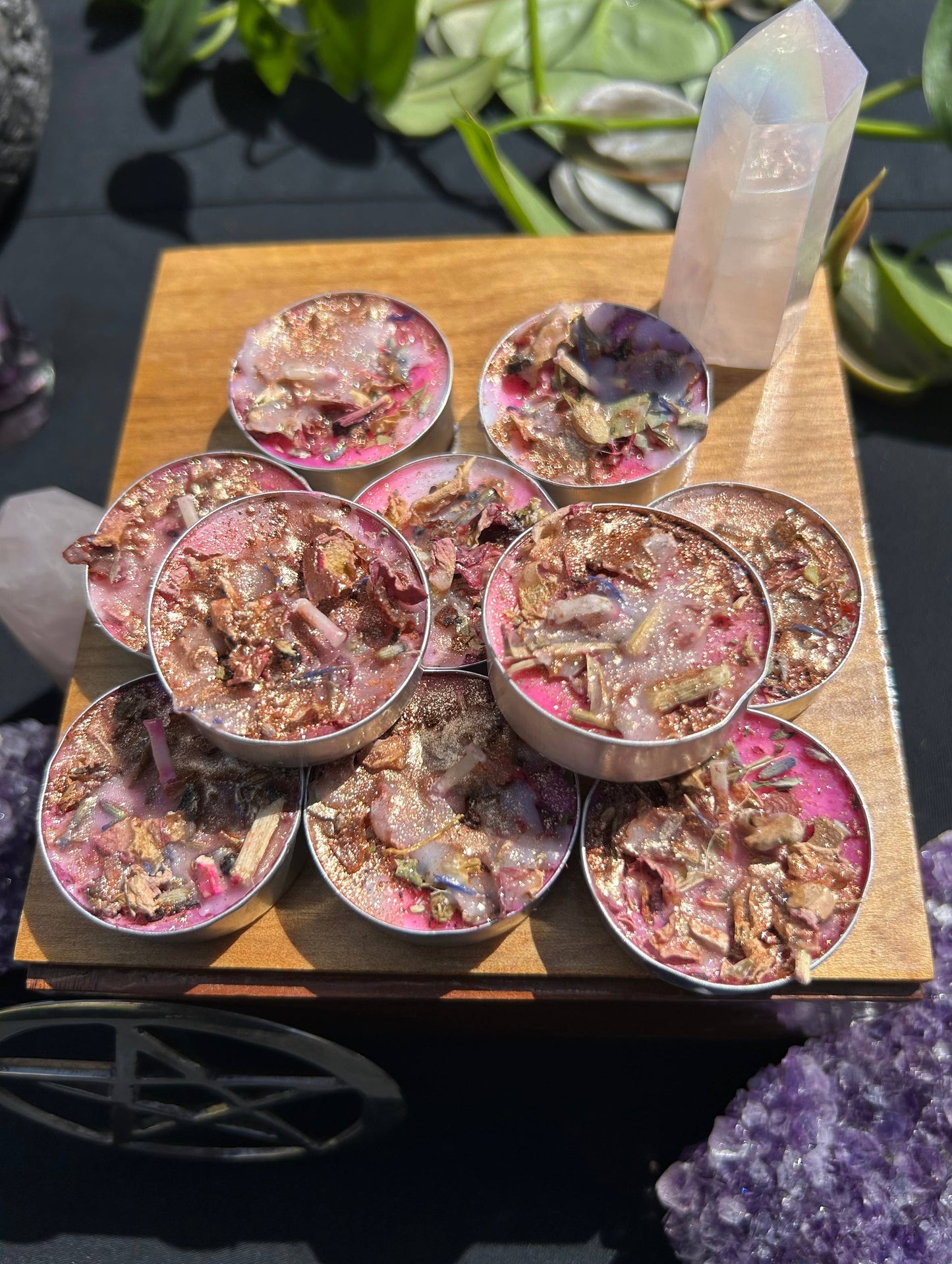Small containers with decorative contents on a wooden board, surrounded by crystals and plants.