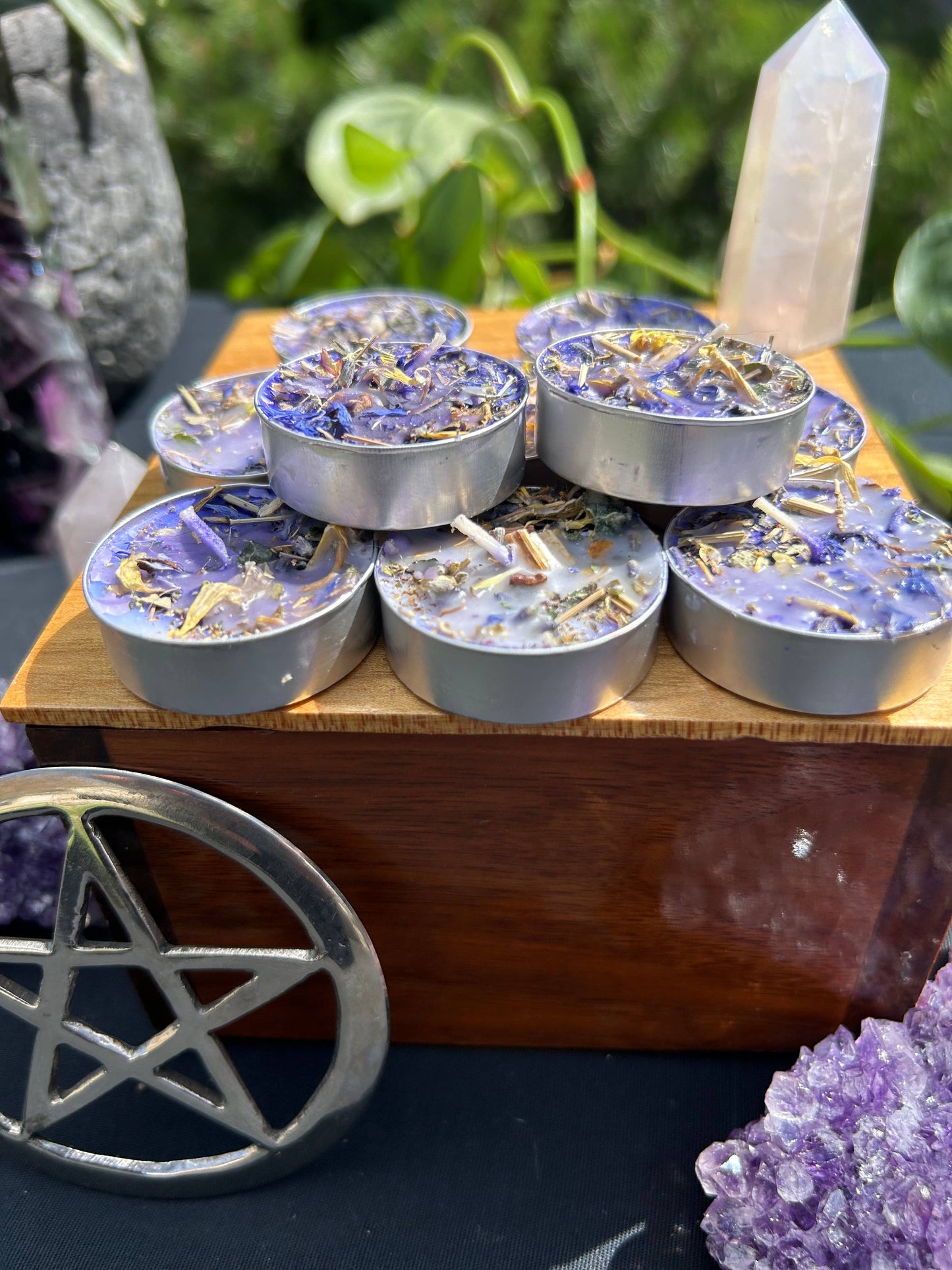 Set of small candles in tin containers on a wooden stand with crystals and a pentacle symbol in the background.